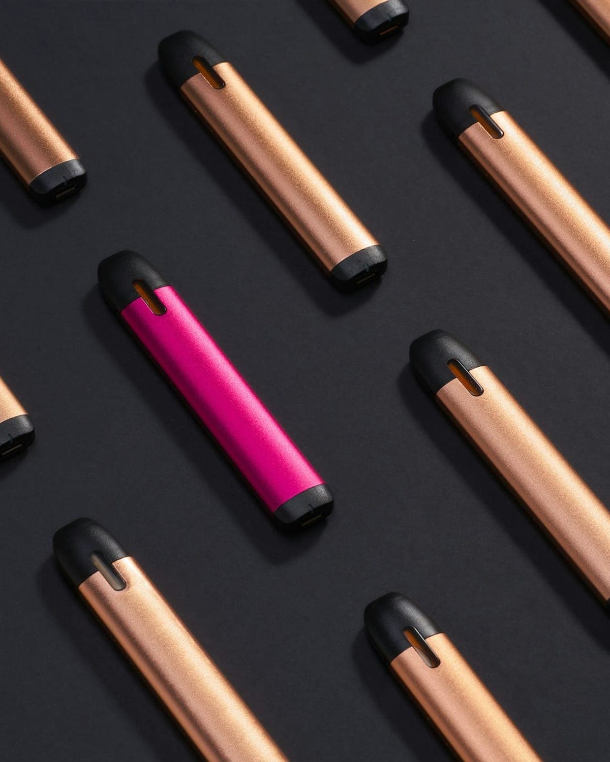Rows of slim disposable vape pens on a dark surface, one in pink