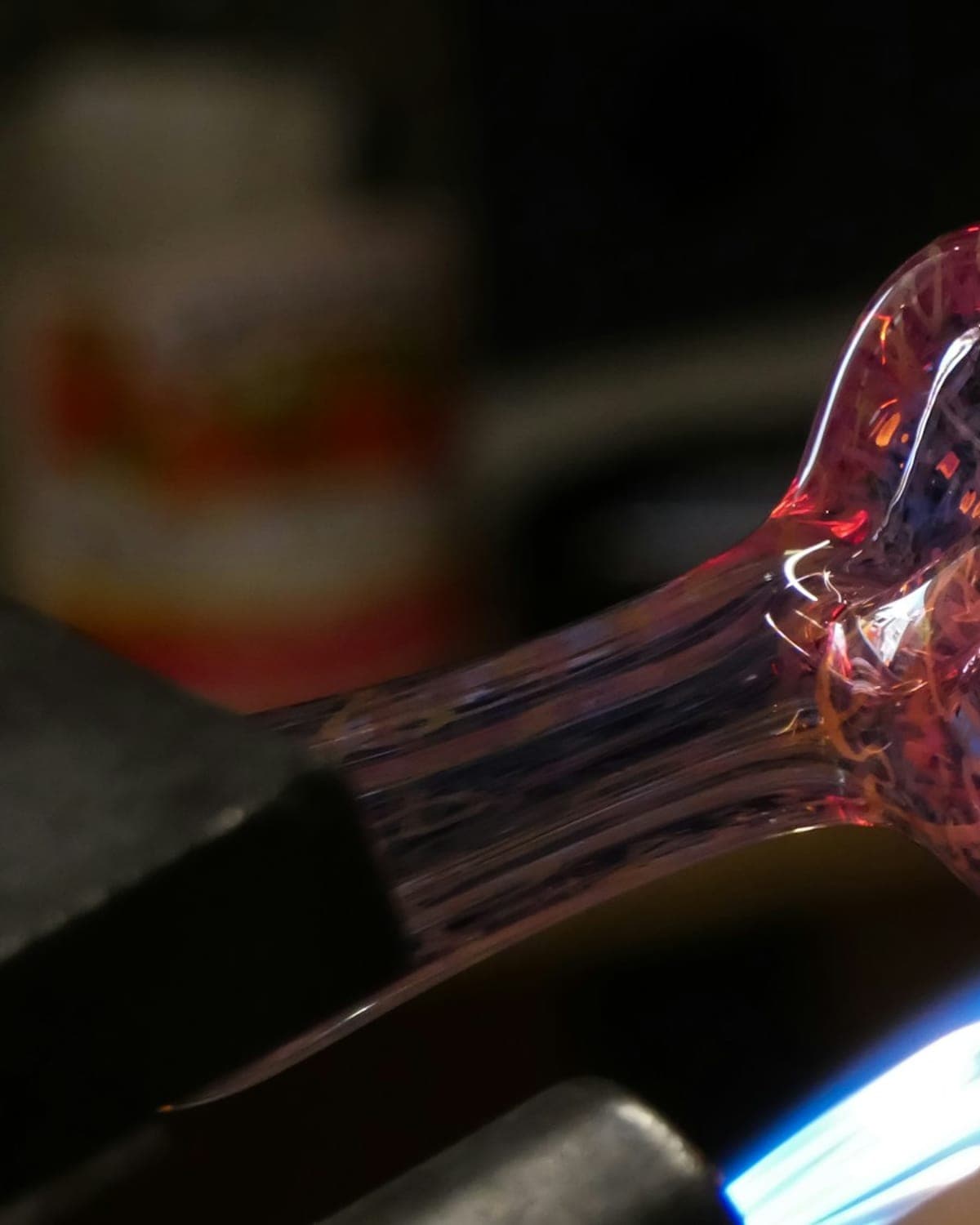 A glassblower shaping a glass piece in a blue torch flame