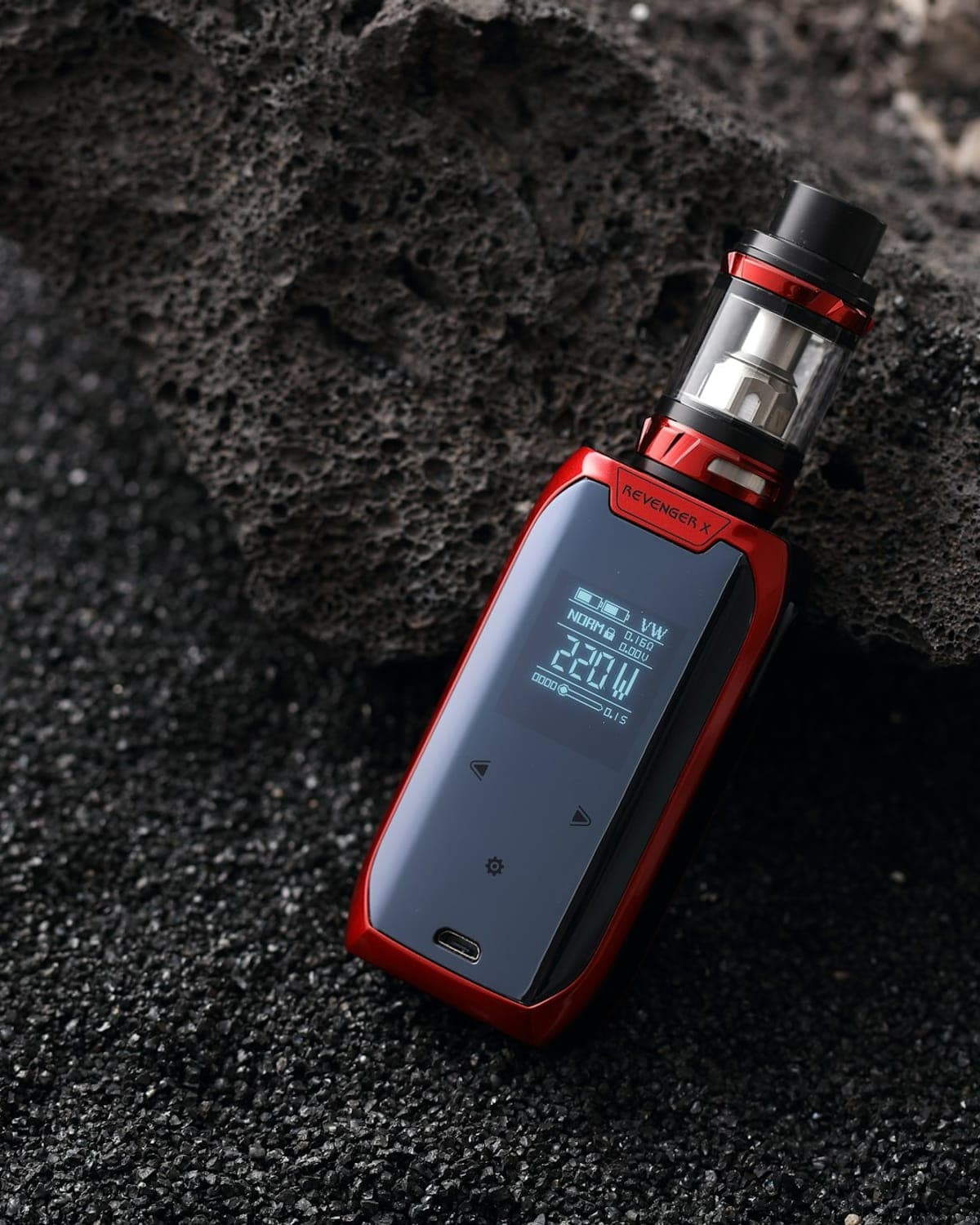 A red box mod with a tank, resting on black volcanic sand