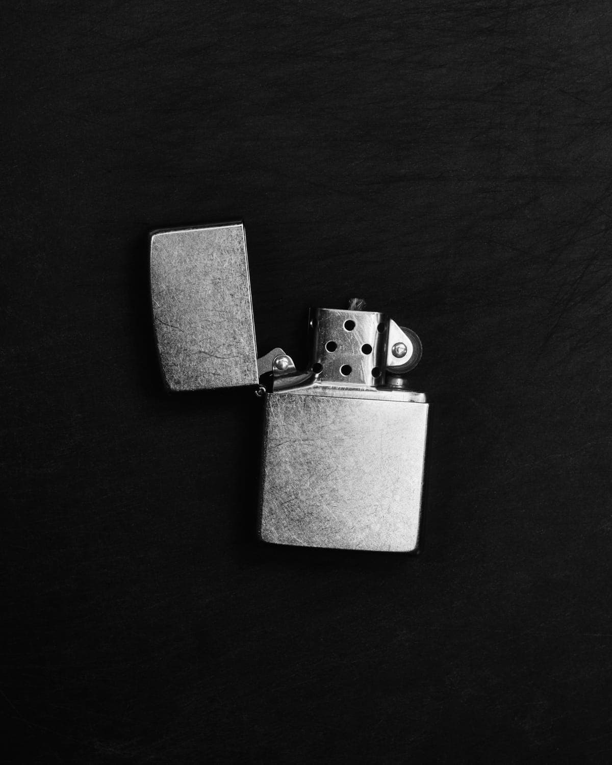 A brushed-steel flip-top lighter, open, on black
