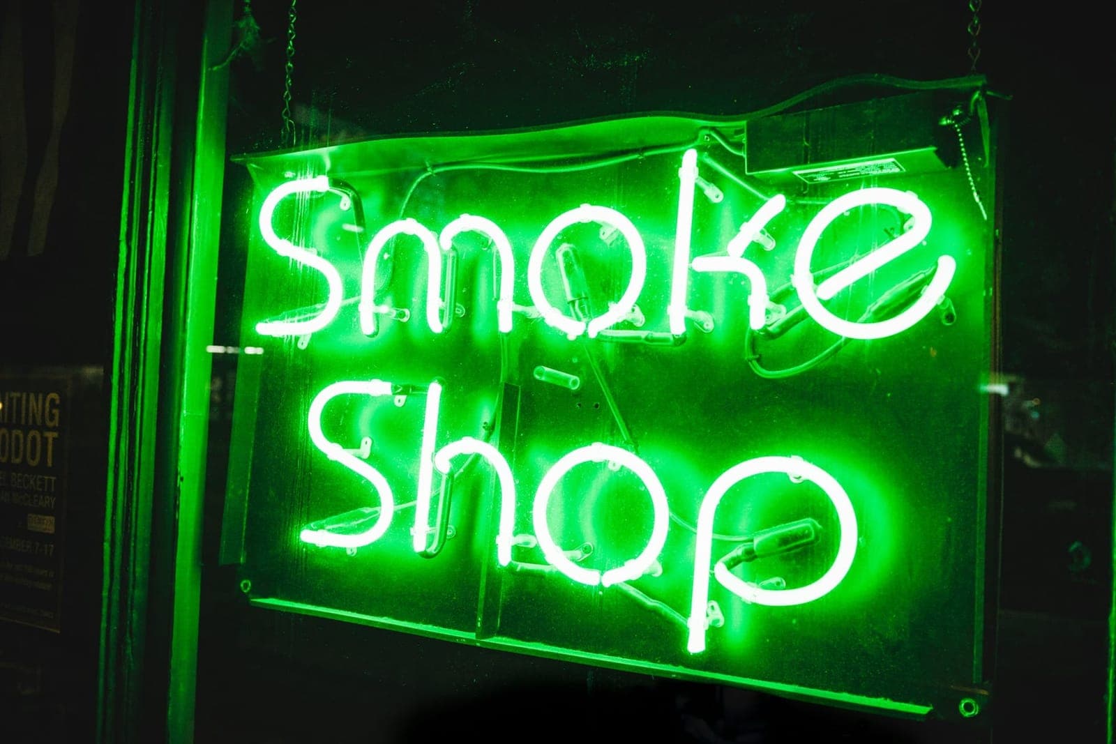 A green neon sign that reads Smoke Shop, glowing in a dark window